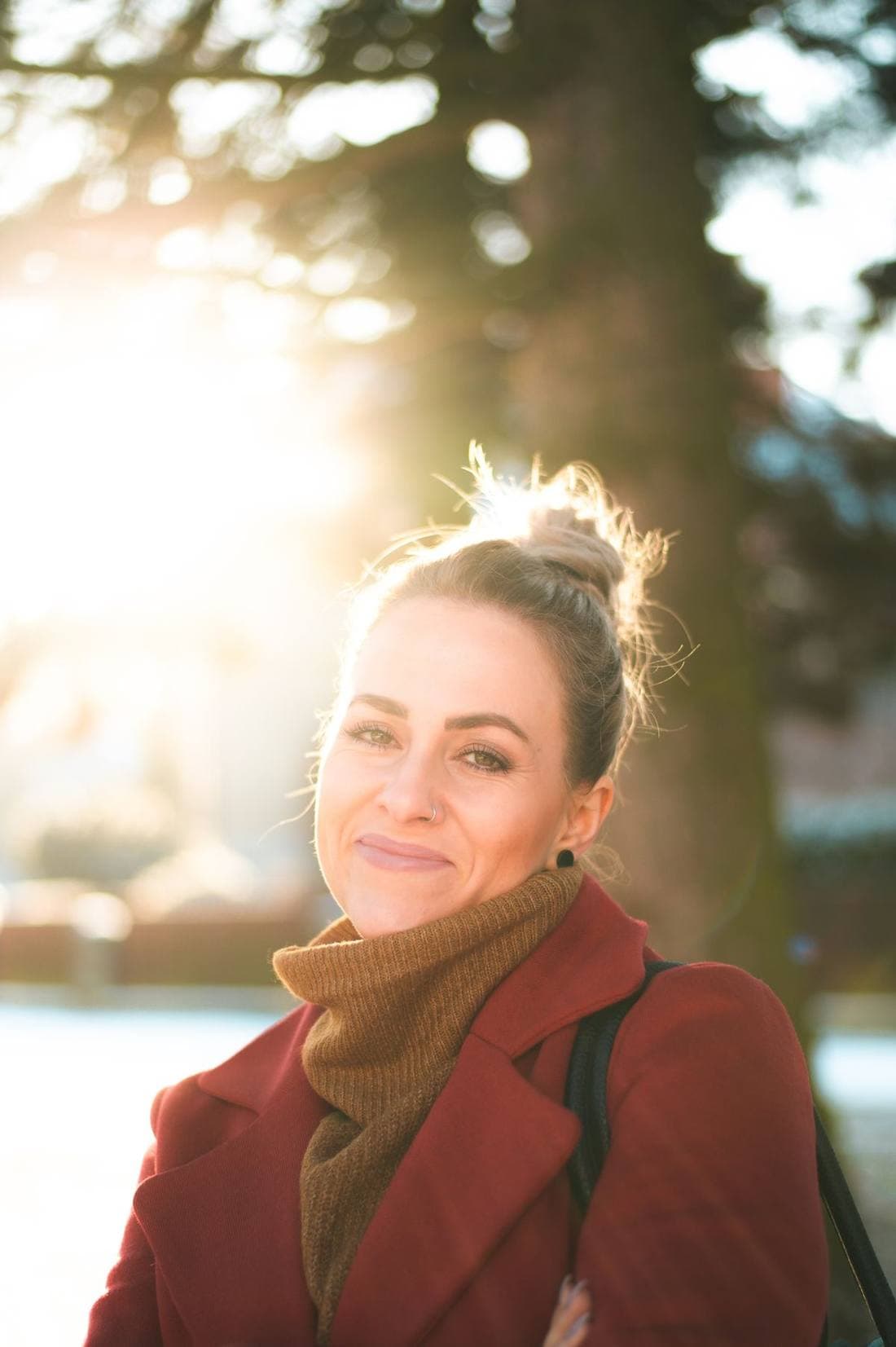 A woman outdoors in low winter sun, half-smiling, backlit.